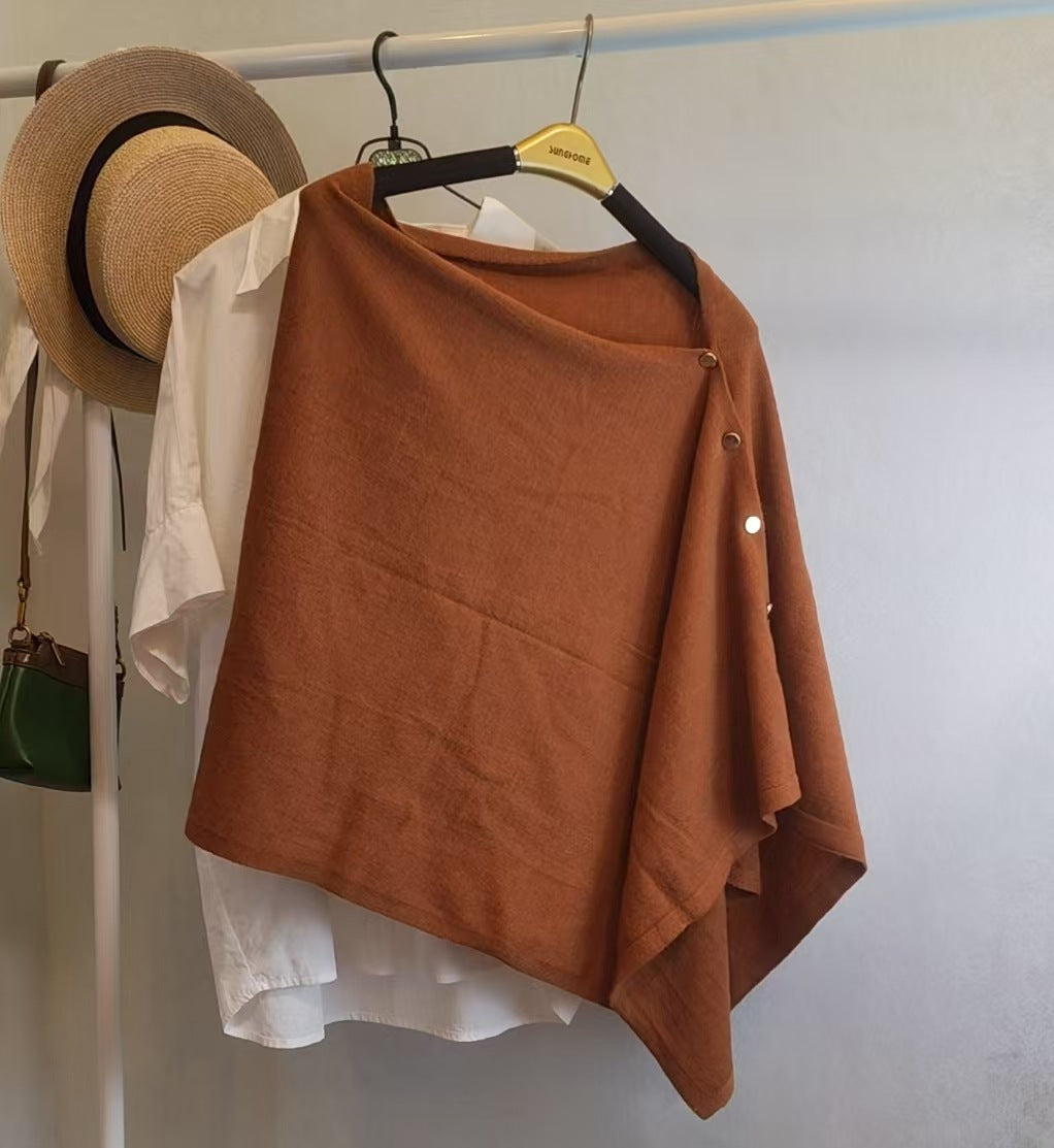 Brick red slouchy knit shawl with side button closure hanging on a rack over a white shirt for autumn warmth.